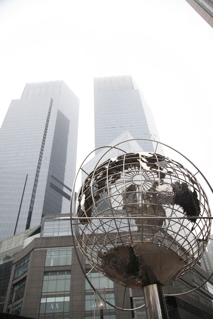 Stainless steel globe statue with towering skyscrapers in New York City.